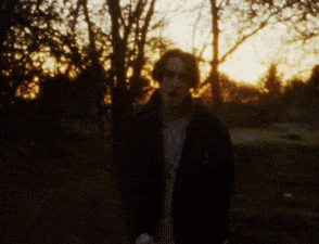 a blurry picture of a man standing in a dark forest at sunset