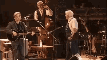 a man is playing a guitar on a stage with other men