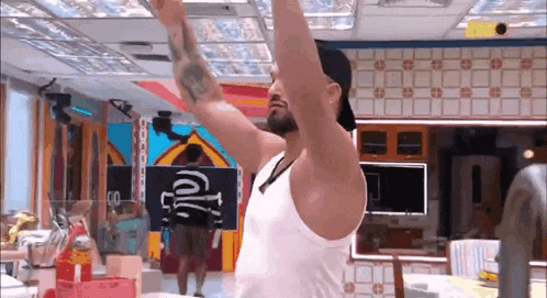 a man in a white tank top is standing in a room with his arms outstretched .