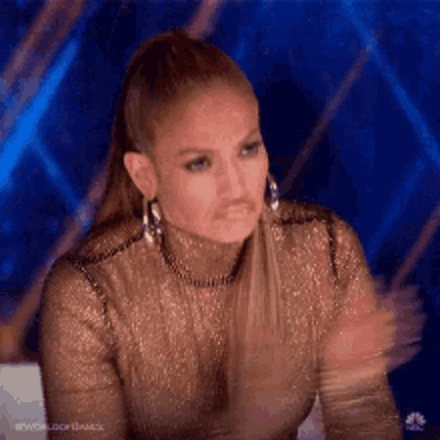 a woman wearing a gold top and earrings is clapping her hands while sitting on a chair .