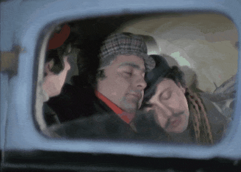 two men are sleeping in a car with a woman looking out the window