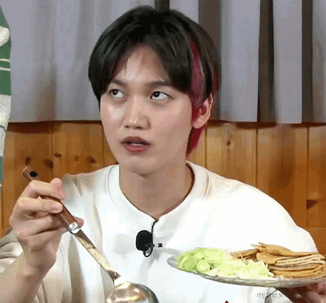 a young man with red hair is eating a plate of food with a ladle .