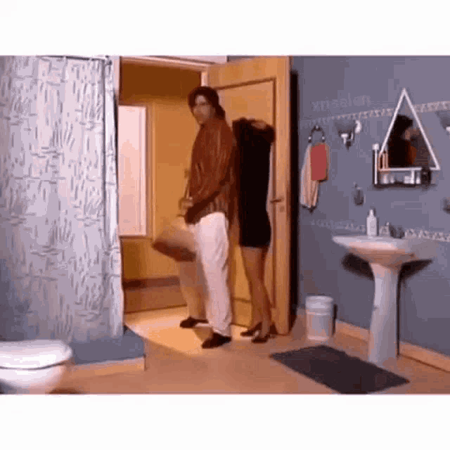 a man and woman are standing in a bathroom next to a toilet and sink .