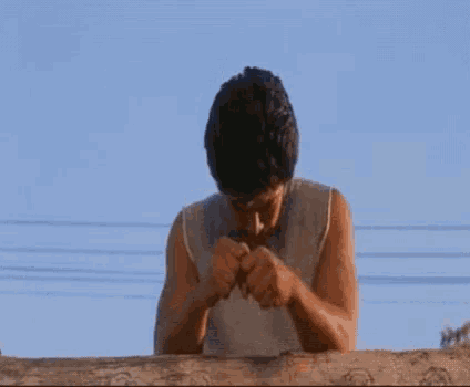 a man is sitting on top of a wooden fence looking down at something .