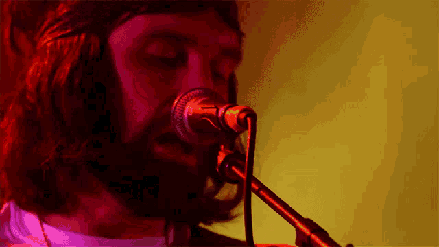 a man with a beard is singing into a microphone with a red light behind him
