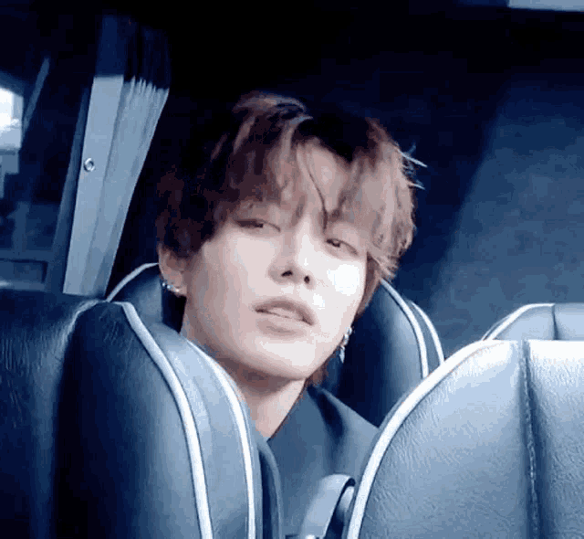 a young man is sitting in a car seat with his eyes closed and his mouth open .