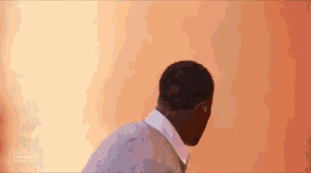 a man in a suit and tie is standing in front of a wall with a blurred background .