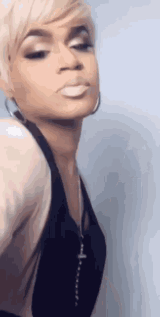 a woman with short blonde hair is wearing a black top and earrings .