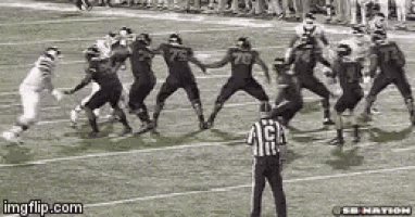 a referee is standing on a football field watching a football game being played .