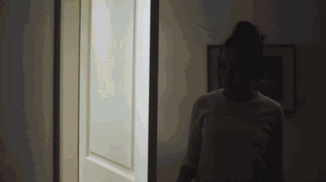 a woman in a white shirt stands in a dark room