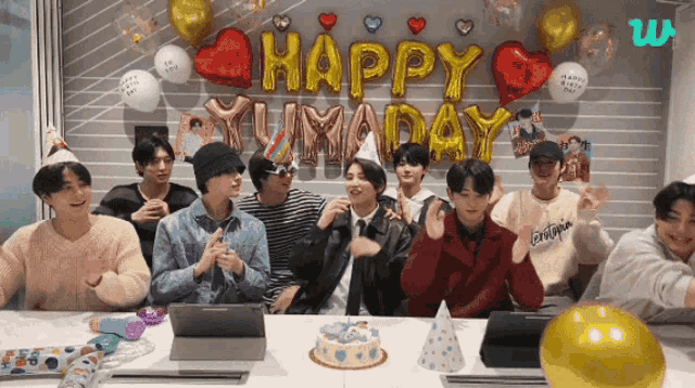 a group of young men are sitting at a table with balloons and a cake that says happy birthday