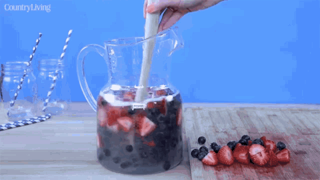 a pitcher filled with strawberries and blueberries is being stirred with a wooden stick and the words country living are on the bottom