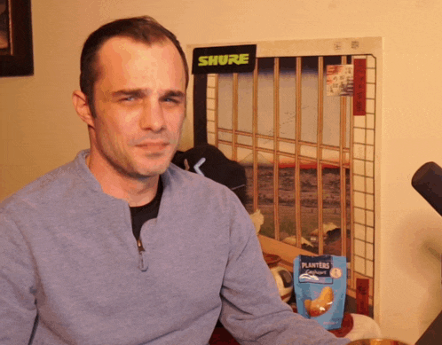 a man sits in front of a shure sign and a bag of planters chips