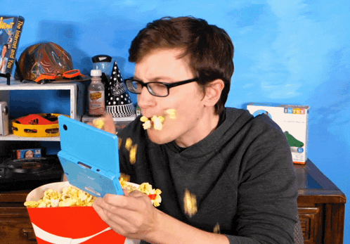 a man is eating popcorn while playing a game on a nintendo ds