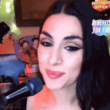 a woman singing into a microphone with a recharge offer for you behind her