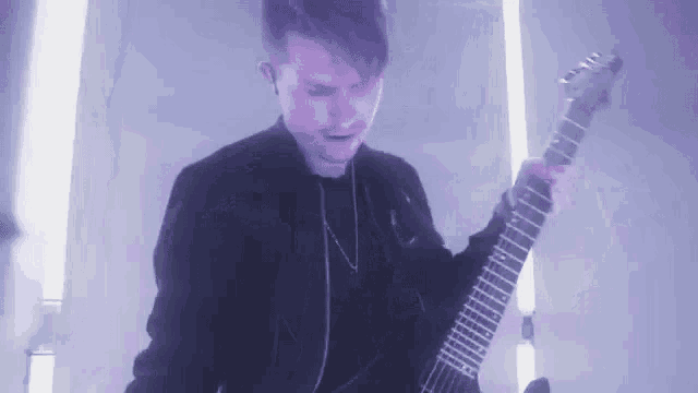 a young man in a black jacket is playing a guitar in a dark room .