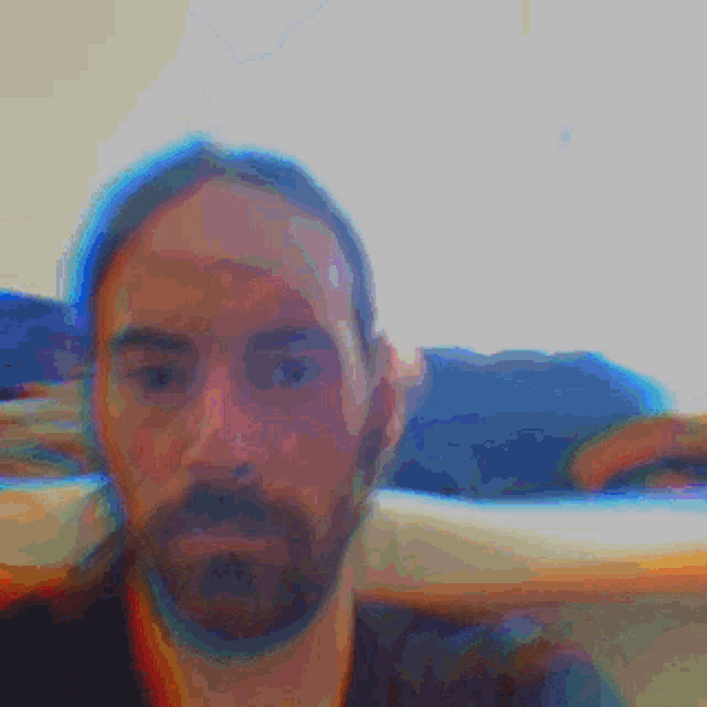 a man with long hair and a beard looks at the camera
