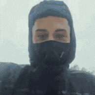 a man wearing a mask and a hooded jacket is standing in the snow .