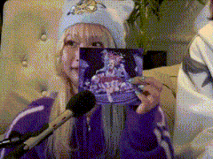 a woman in a blue hat is holding a picture in front of a microphone while wearing a purple jacket .