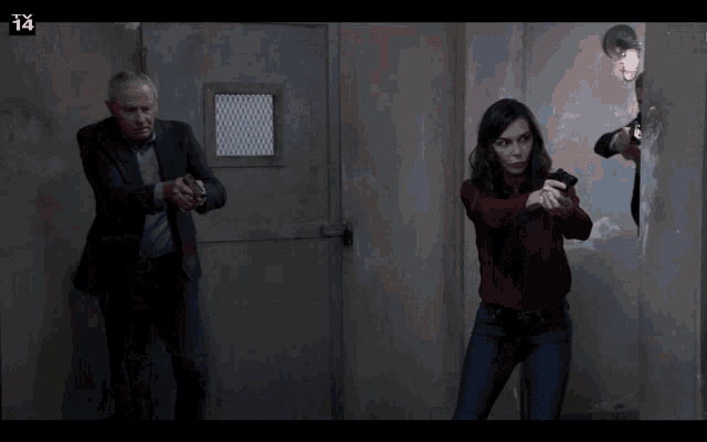 a man in a suit and a woman in a red shirt are holding guns in a dark room with the number 14 on the bottom