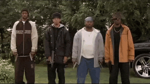a group of men are standing next to each other in front of a car holding guns .