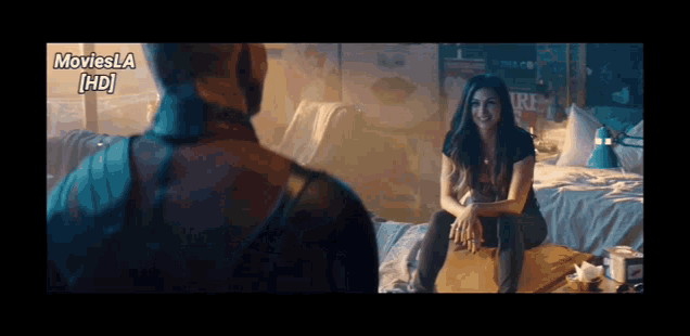 a woman is sitting on a bed talking to a man in a movie