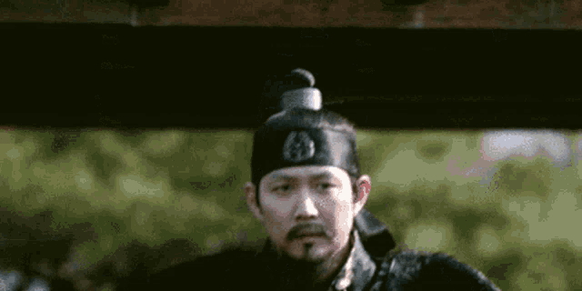 a man with a beard and mustache is wearing a black hat and a black robe .