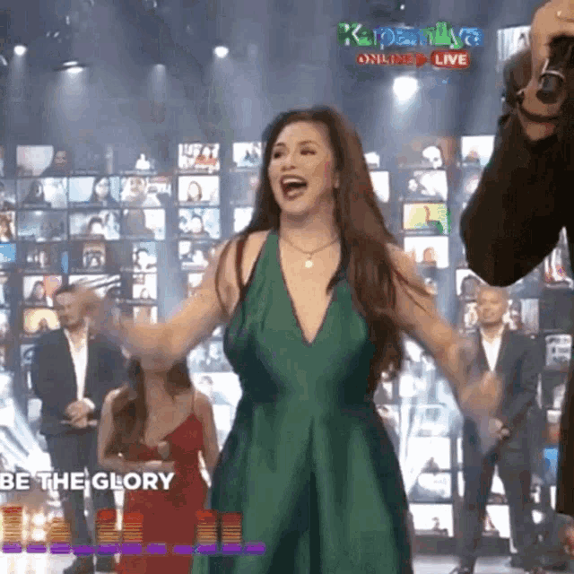 a woman in a green dress is on a stage in front of a sign that says " be the glory "