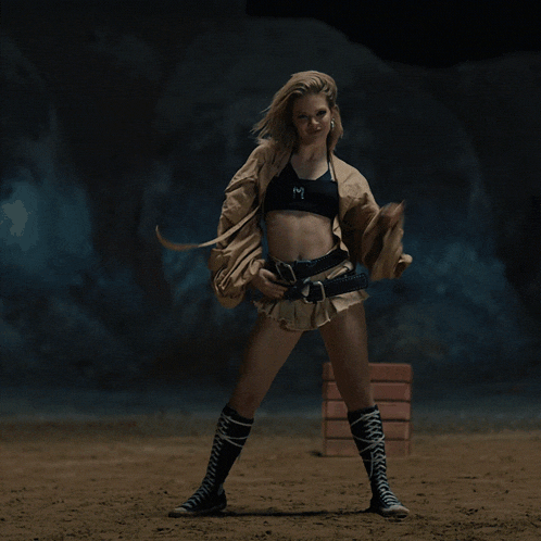 a woman in a crop top and shorts is standing on a dirt field