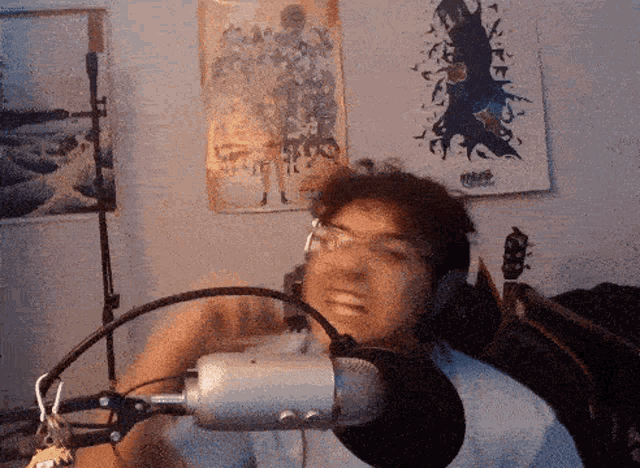 a man wearing headphones stands in front of a microphone in front of a wall with posters on it