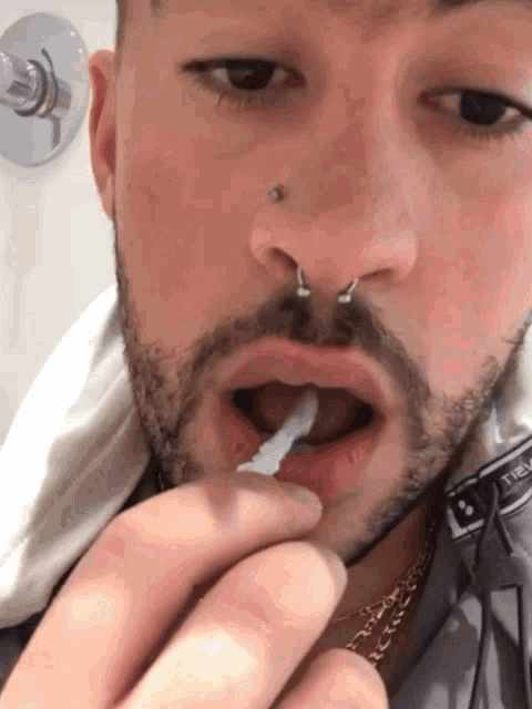 a man with a nose ring is brushing his teeth with a white toothpaste