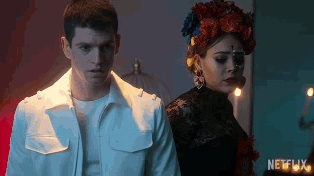 a man in a white jacket stands next to a woman in a black dress with netflix written on the bottom right