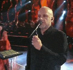 a man singing into a microphone with a crowd behind him