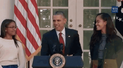 a man in a suit and tie is standing at a podium with two girls behind him .