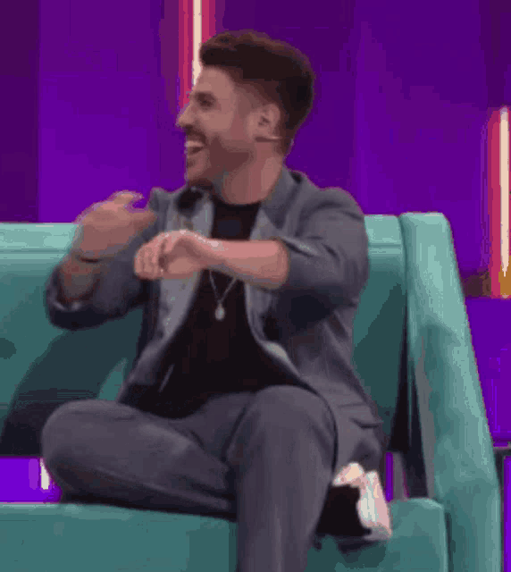a man in a suit is sitting on a blue couch with his arms crossed and smiling .