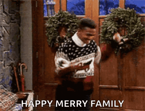 a man in a sweater is standing in front of a door holding a wreath and a phone .