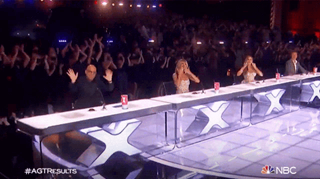 a group of people sitting at a table with a x on it and a nbc logo in the corner