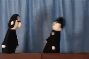 two black and white stuffed animals are standing next to each other on a stage in front of a blue curtain .