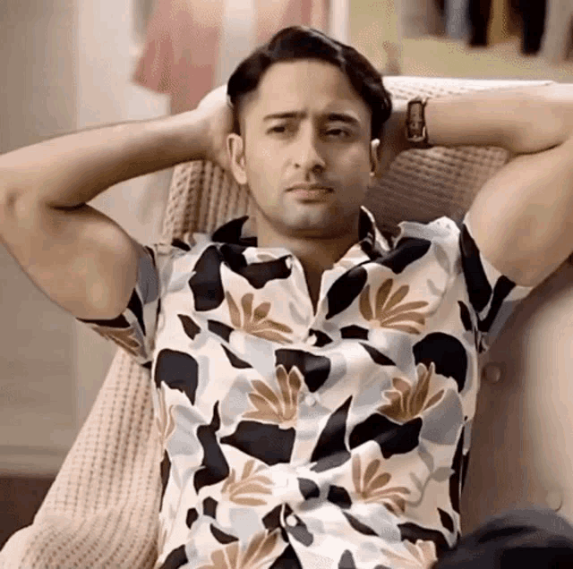 a man in a floral shirt is sitting on a chair with his hands behind his head .