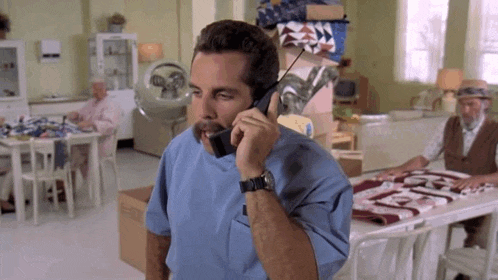 a man in a blue scrub top is talking on a cell phone in a room .