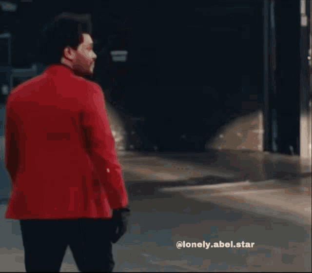 a man in a red jacket is standing in a dark room with a caption that says lonely.abel.star