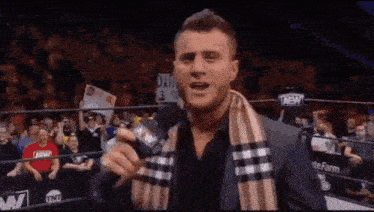 a man in a suit and scarf is holding a microphone in front of a crowd of people .