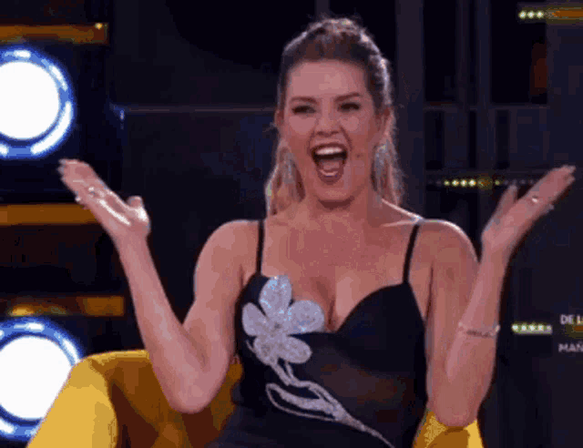 a woman in a black dress is sitting in a yellow chair with her hands in the air