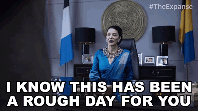 a woman in a blue dress is sitting at a desk and says i know this has been a rough day for you