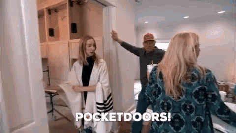 a man and a woman are standing in a room talking to each other . the woman is wearing a poncho .