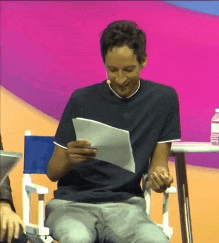 a man in a black shirt is sitting in a chair reading a piece of paper