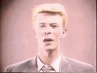 a man in a suit and tie is looking at the camera with a pink background .