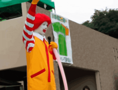 a clown in a mcdonald 's costume is holding up a green sign