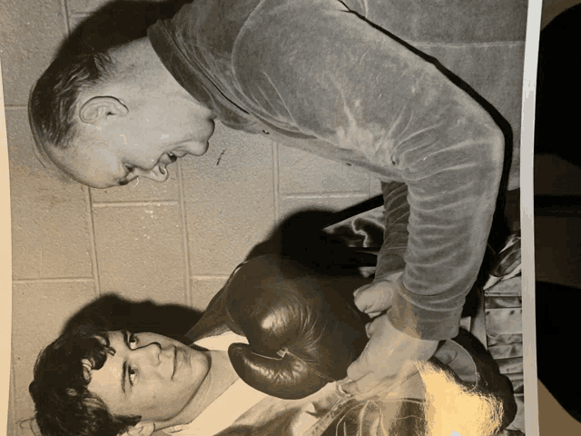 a black and white photo of a man wearing boxing gloves talking to another man