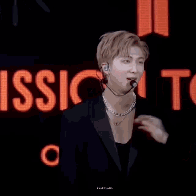 a man in a suit and a necklace is standing in front of a microphone on a stage .
